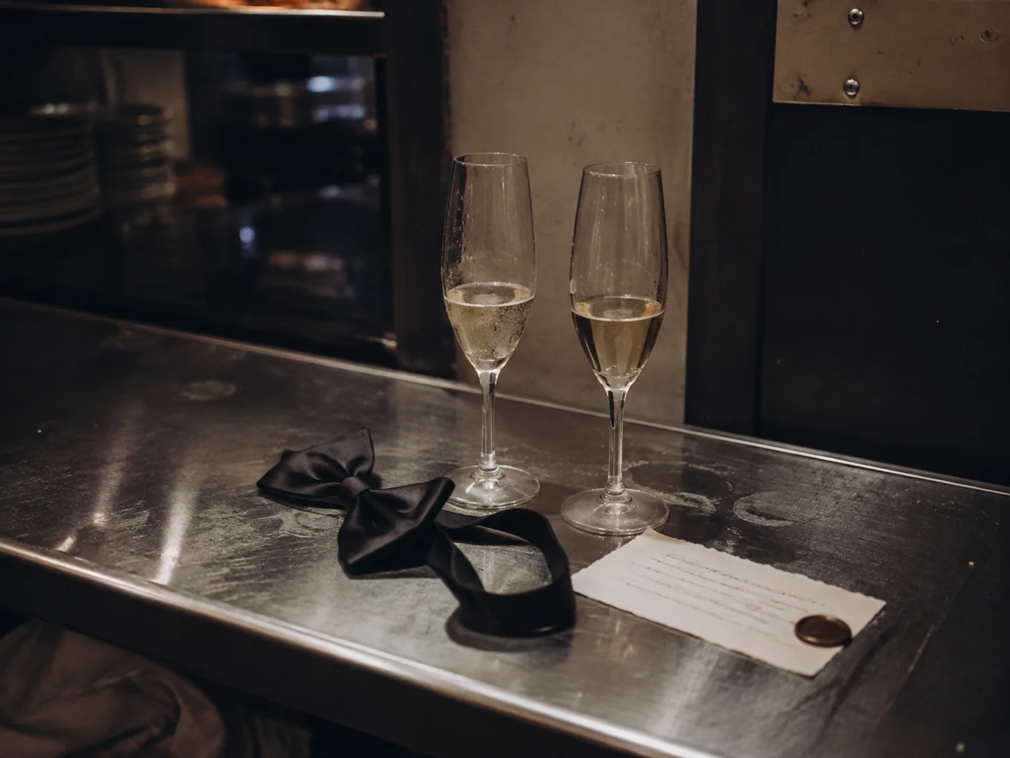 Two champagne glasses and a loosened bow tie left on a steel counter