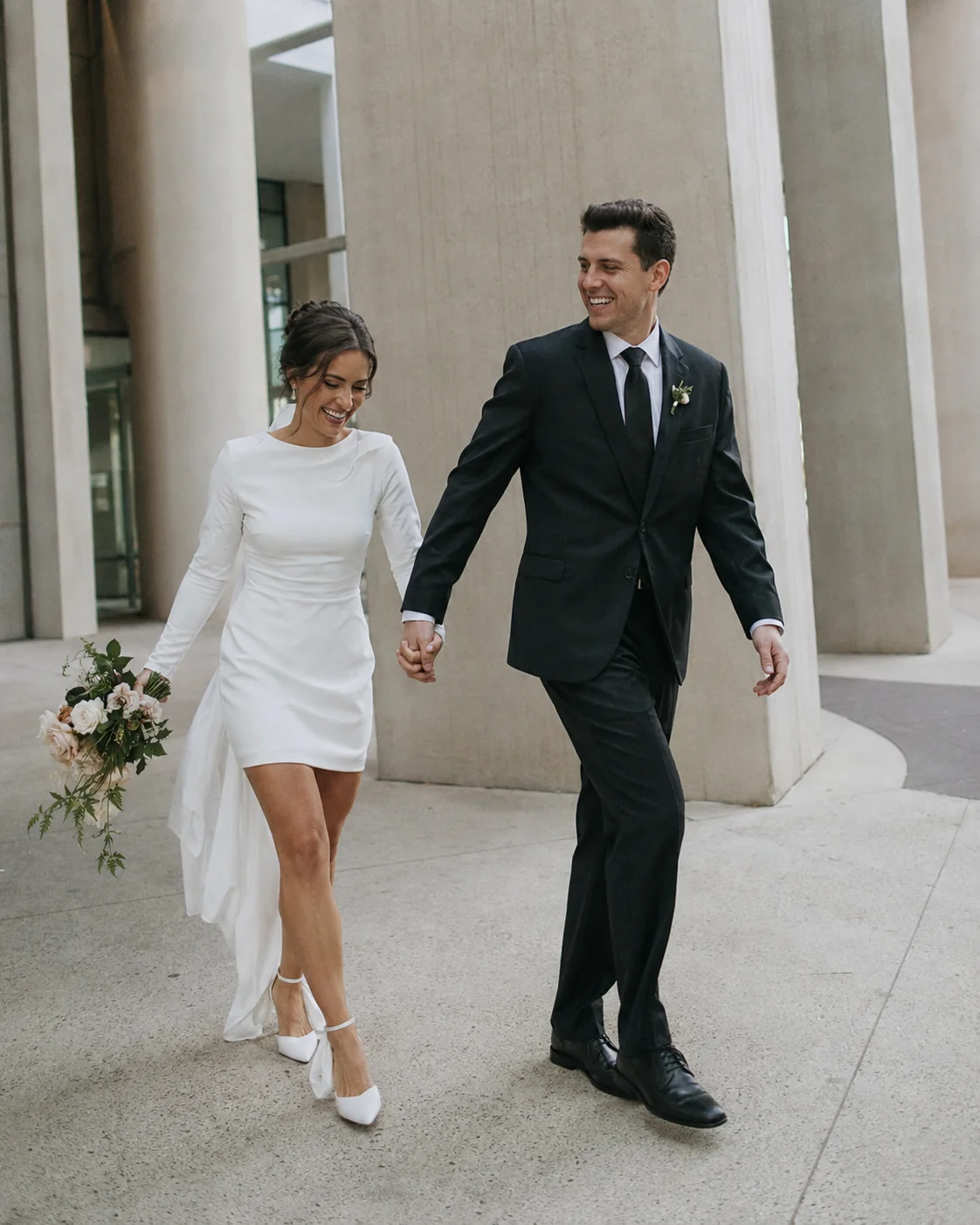 A newly married couple walking together between concrete columns